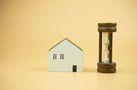 Hourglass with wood home on a yellow background. The concept for business deadline times or building...