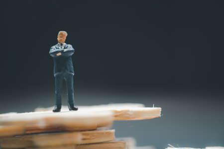Miniature people businessman standing above jigsaw puzzle piece stack. The concetp of investment analyst or investment in solve puzzles to find a business solution.の写真素材