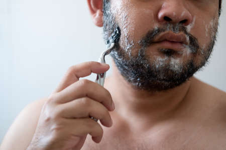 Cropped photo of handsome male shaving while using foam and razorの写真素材