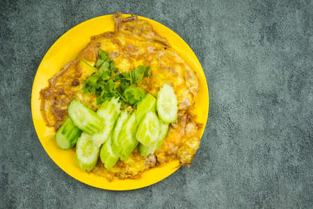 Above view of omelet served with cucumber and cilantro in yellow plate. Omelet egg fry popular traditional Thai homemade style food.の写真素材