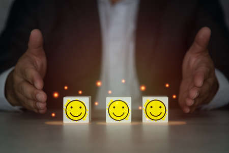 Man with open hands for show wooden cube block shape with icon happy face. The best excellent business servicesの写真素材