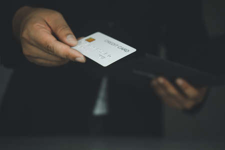 Businessman in a black classic suit holding a white plastic credit card in the studio on a dark background. shopping conceptの写真素材