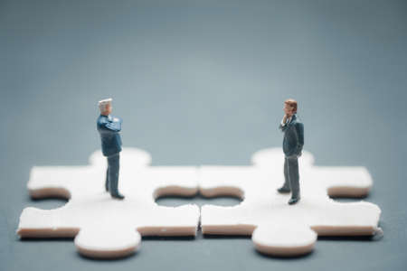 Close up of businessman miniature standing on jigsaw pieces and standing face to face having struggle for leadership on businessmeeting because of business competition, business competition.の写真素材