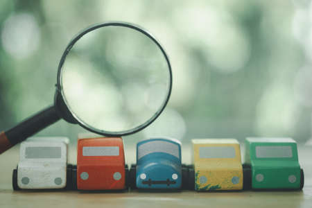 A row of toy car and magnifying glass placed on top. Technical inspection and car search concept