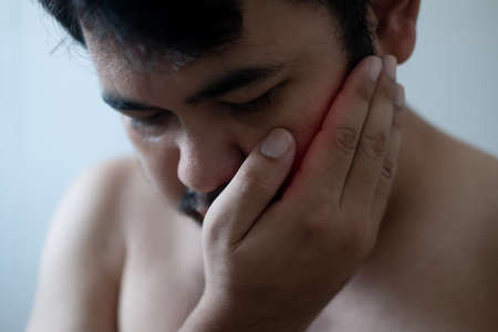 Close up of young man touching his face and closing eyes with expression of horrible suffer from...