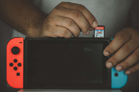 Samut Prakan, Thailand - July 24, 2021 : Close up of man inserting The Legend of Zelda: Skyward Sword HD video game cartridge into a Nintendo Switch console.のeditorial素材