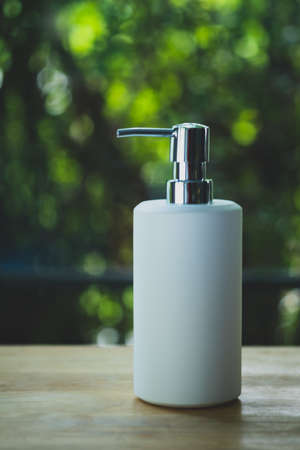White ceramic pump bottle for liquid soap or shampoo on wood table in homeの写真素材