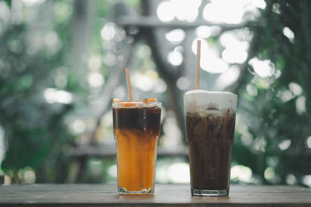A glass of coffee mixed with orange juice places with iced Mocha coffee on a wooden table at garden...