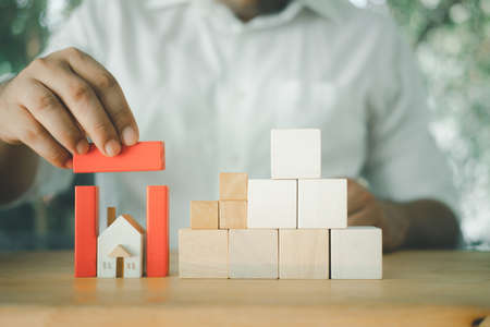 Businessman hand protects home with red block roof.