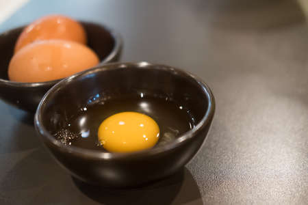 Fresh raw egg yolk and white yolk for eating with shabu and sukiyaki in a black bowl. Japanese...