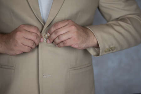 Man is buttoning the buttons on the cream suit. Getting ready for formal event.の写真素材