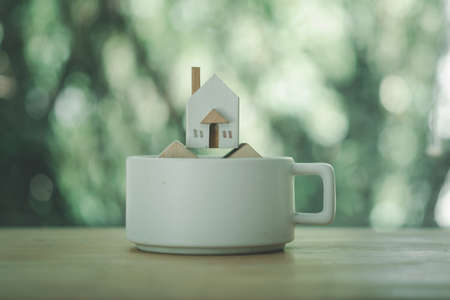 Miniature wooden home placed on the white ceramic cup. Home care, Home for sale concept.の写真素材