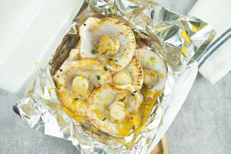 Grilled scallops topped with butter, garlic and onion served in foil paper placed on box