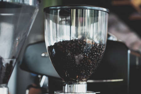 Fresh dark roasted arabica coffee bean in electric coffee grinder machine in the cafeの写真素材
