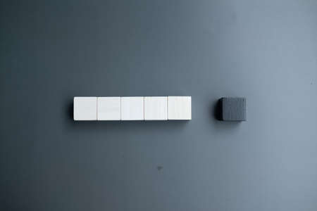 Arranging a row of five white blank wooden blocks and one black blank wooden block with copy space...