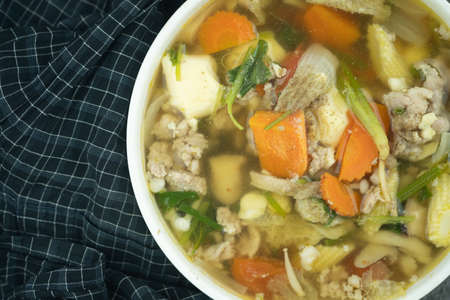 Clear vegetable soup with minced pork on white bowl. Top view