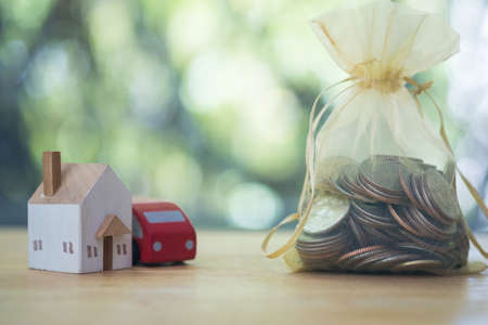 Car with house placed beside the golden bag coin on the wooden floor in business idea and profit concept. Savings money for the future concepts.の写真素材