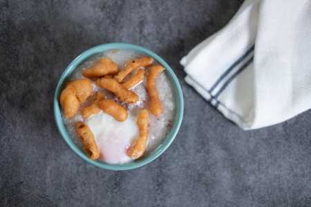 Top view of rice porridge with minced pork, soft-boiled egg and deep-fried dough stick in bowlの写真素材