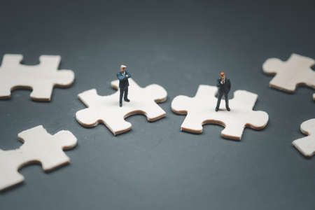Two miniature people businessman standing on incomplete jigsaw puzzles. Conceptual photos of...