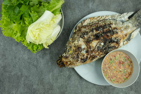Salt crusted grilled fish with spicy dip and fresh vegetables on a black gackgroundの写真素材