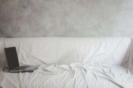 Laptop or notebook on a white sofa in the morning at home. Working from home during coronavirus pandemicの写真素材