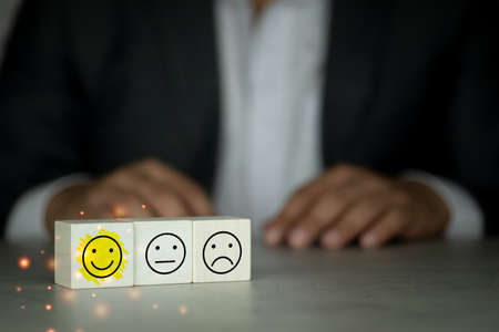 Wooden blocks with the face symbol on the table with businessman in black suit background, satisfaction and best excellent services rating. The concept of Excellent quality evaluationの写真素材