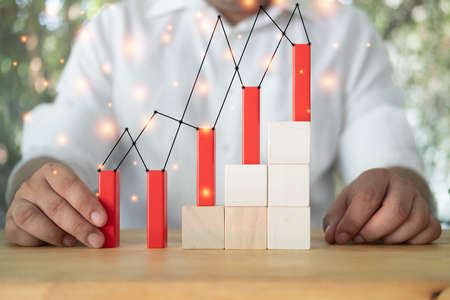 Cropped view of man hand putting red wooden block like a graph on wooden blocks in the shape of a...