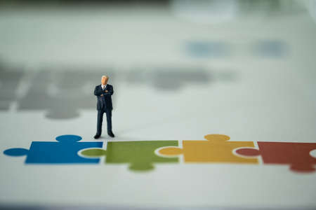 Miniature people businessman thinking and standing on a paper jigsaw. Key person for business success strategy conceptの写真素材