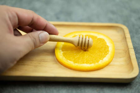 Hand put honey stick on a slices of sliced orange on wood trayの写真素材