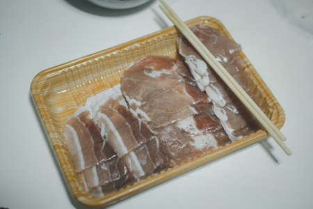 Thinly-sliced raw pork loin in packaging tray ready to cook.の写真素材