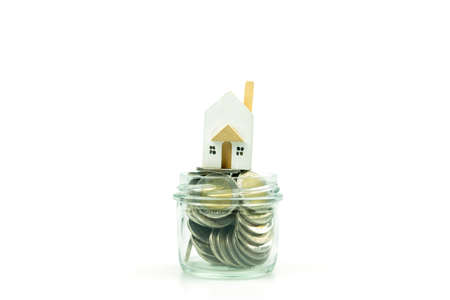 Wood house model placed a stack of Thai coins money in glass on a white background. Savings money concept.の写真素材