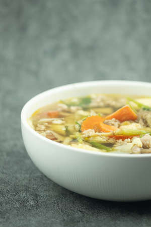 Clear soup with vegetables and minced pork in white bowlの写真素材