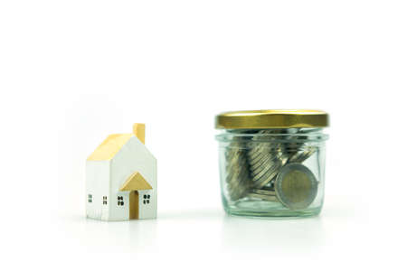 Coin in glass jar with wood house on a white background. Saving money or mortgage concept.の写真素材