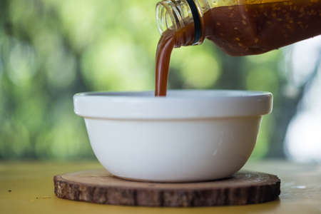 Close up of pour sukiyaki sauce with sesame seeds from the bottle on bowlの写真素材