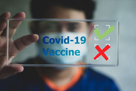 A young man with face mask show information of Coronavirus vaccine survey form with checkboxes, marked with Yes or No. Covid-19 vaccine and medical conceptの写真素材