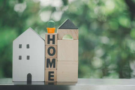 Wood block with HOME text and house model with miniature cactus on an against nature background with copy space for text. Housing and real estate concept.の写真素材
