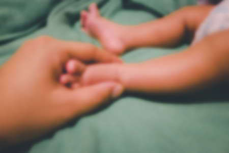 Blur background of father holds the feet of the newborn baby in his hand.の写真素材
