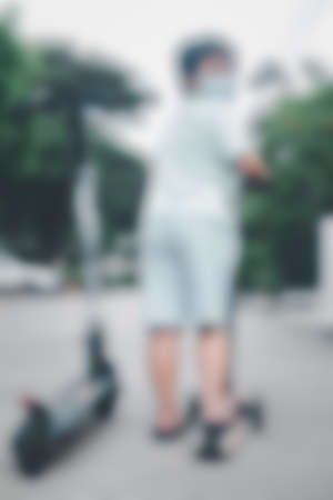 Blur background of back young boy riding one wheeled push scooter