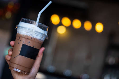 Close up young Asian man hand holding takeaway plastic cup of delicious iced coffee over bokeh...