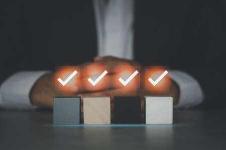 a businessman with clasped hands behind check mark on an empty wood block. Checklist or to do list in business conceptの写真素材