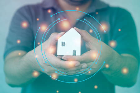Man hand hold mini wood house model protecting with a virtual digital interface. The concept of home insurance.の写真素材