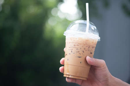 A man holding a plastic glass of Iced latte coffee against nature backgroundの写真素材