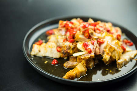 Crispy pork dressing with lime garlic and chili sauce salad on black plateの写真素材