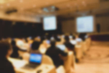 Blurred image of people sitting in conference room for profession seminar, in large hall with screen and projector for showing information.の写真素材