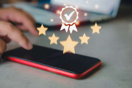 Hand use a smartphone phone and showing the sign of the top service quality assurance, guarantee, standards, ISO certification and standardization concept.の写真素材