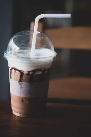 A plastic glass of iced coffee with milk on a wooden table.