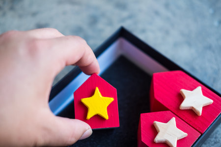 Hand choosing wood red house model with yellow star from many homes. Searching for perfect property in high demand housing boom, choosing best house, making right decision on home investment conceptの写真素材