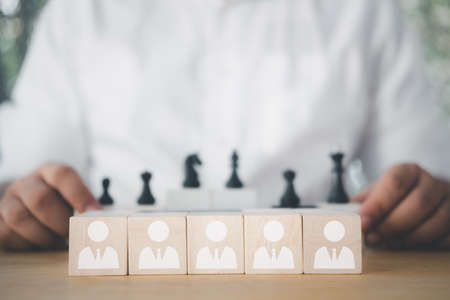 Wooden blocks with white human icons and businessman looking black chess. Leadership and teamwork...