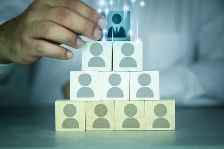 Businessman arranging wooden block with icon of leader person (CEO) on top of many staff icons. The concept of business organization structure and team buildingの写真素材