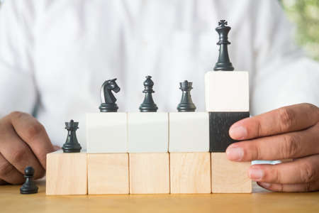 Chess standing on a pyramid of wooden building blocks. Career ladder concept, Business hierarchy and man choose black wood blockの写真素材